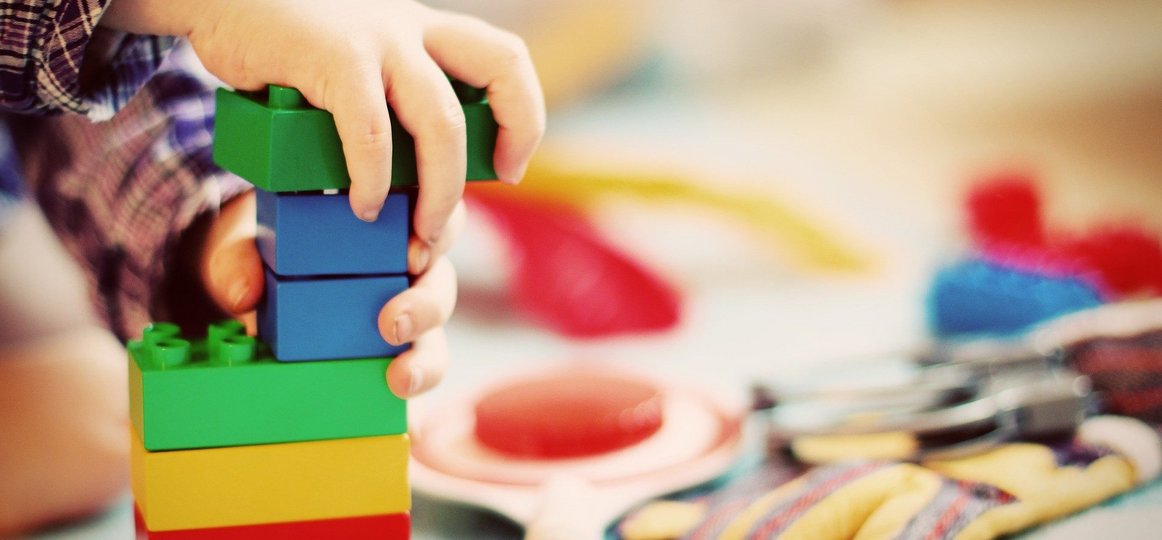 Kind steckt bunte Legosteine zu einem Turm zusammen (Foto: FeeLoona auf Pixabay)